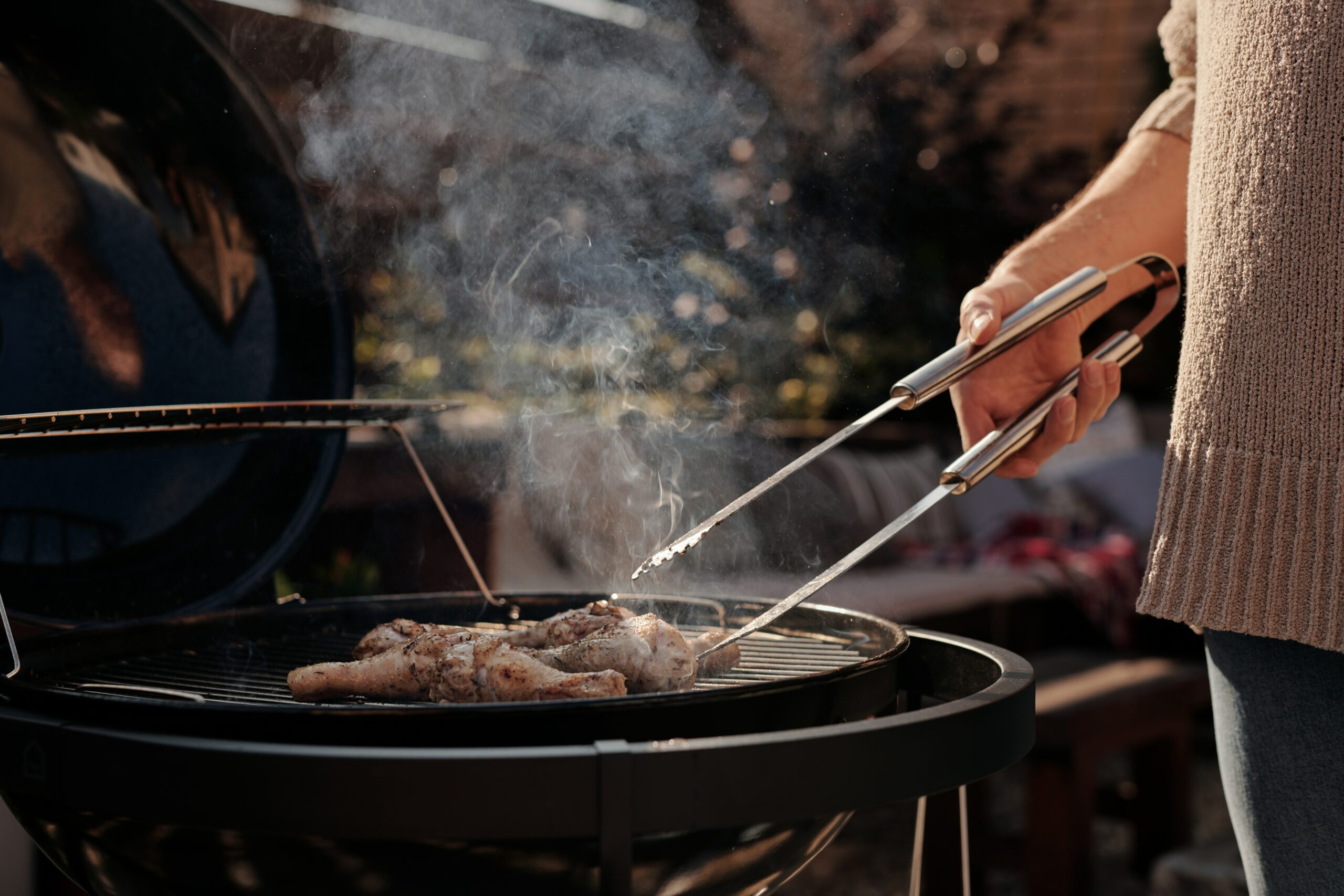 Eine Frau wendet ein Stück Fleisch auf einem Holzkohle Kugelgrills mit einer Grillzange.