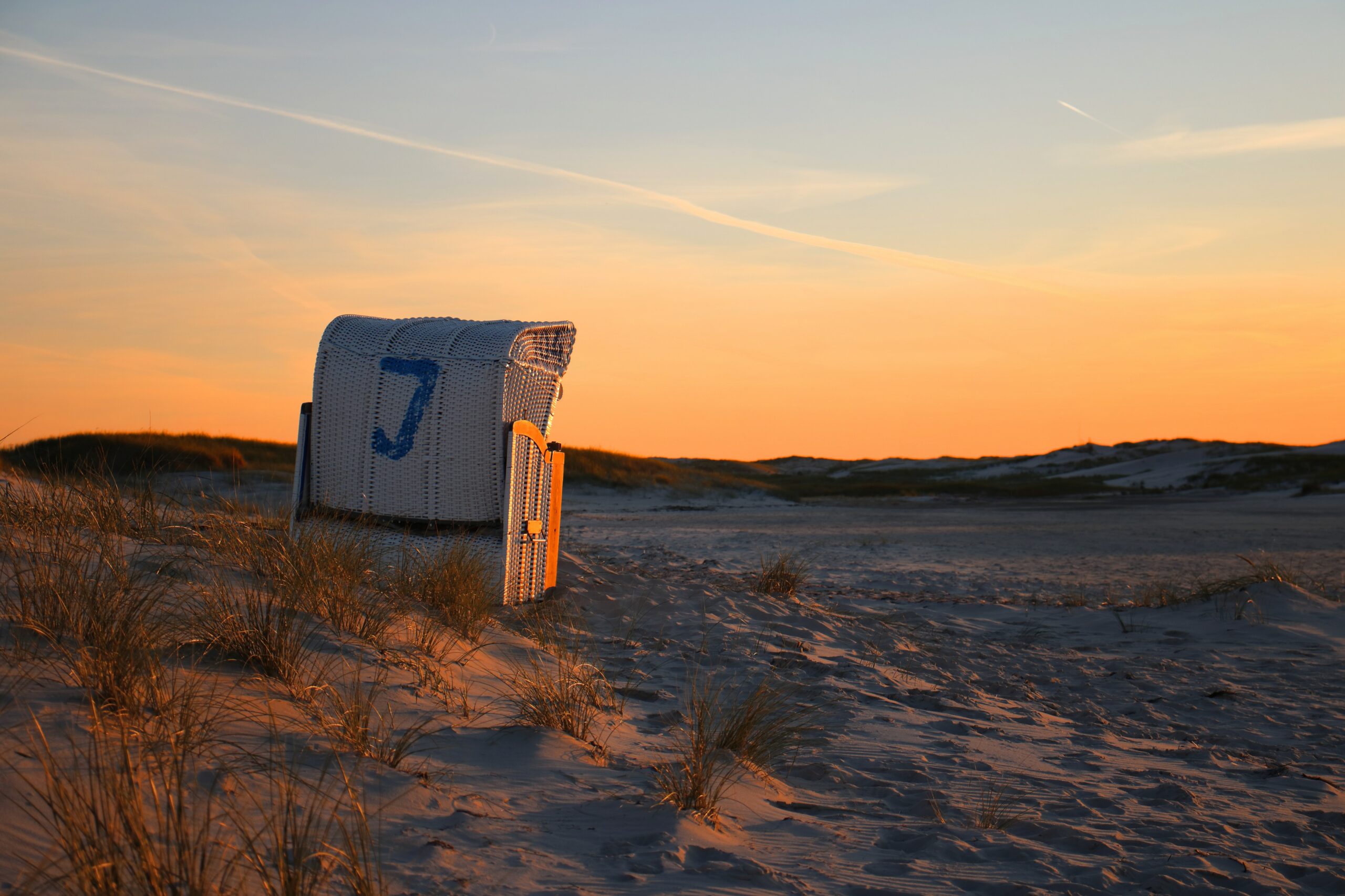 Ein Strandkorb steht in den Dünen der Himmel hinter dem Strandkorb ist rot verfärbt vom Sonnenuntergang