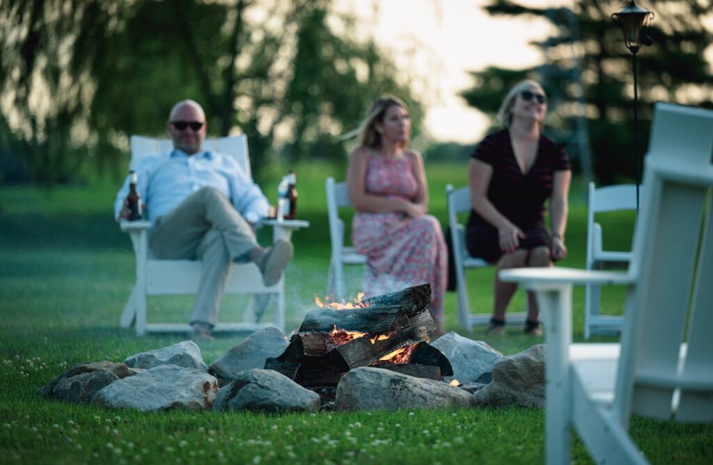 Gartenstühle stehen auf dem Rasen zwichen den Gartenbstühlen brennt ein Lagerfeuer