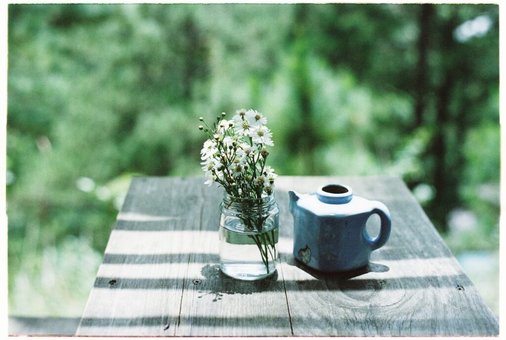 Auf einem Tisch der im Garten steht, steht eine Vase mit Blumen und eine Teekanne