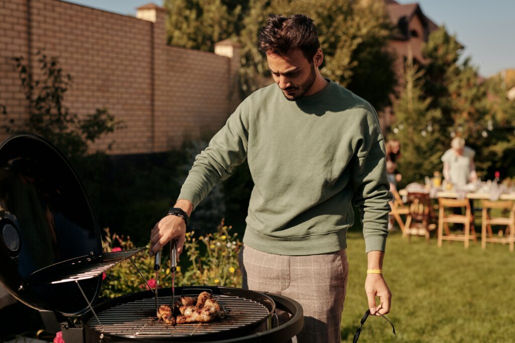 Junger Mann steht an einem Kugelgrill und grillt ein Stück Fleisch