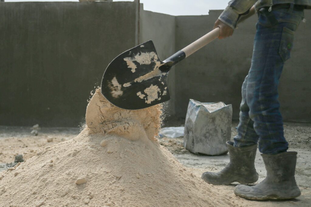 Auf einer Baustelle wird mit einer Schaufel Sand auf einen Haufen geschaufelt