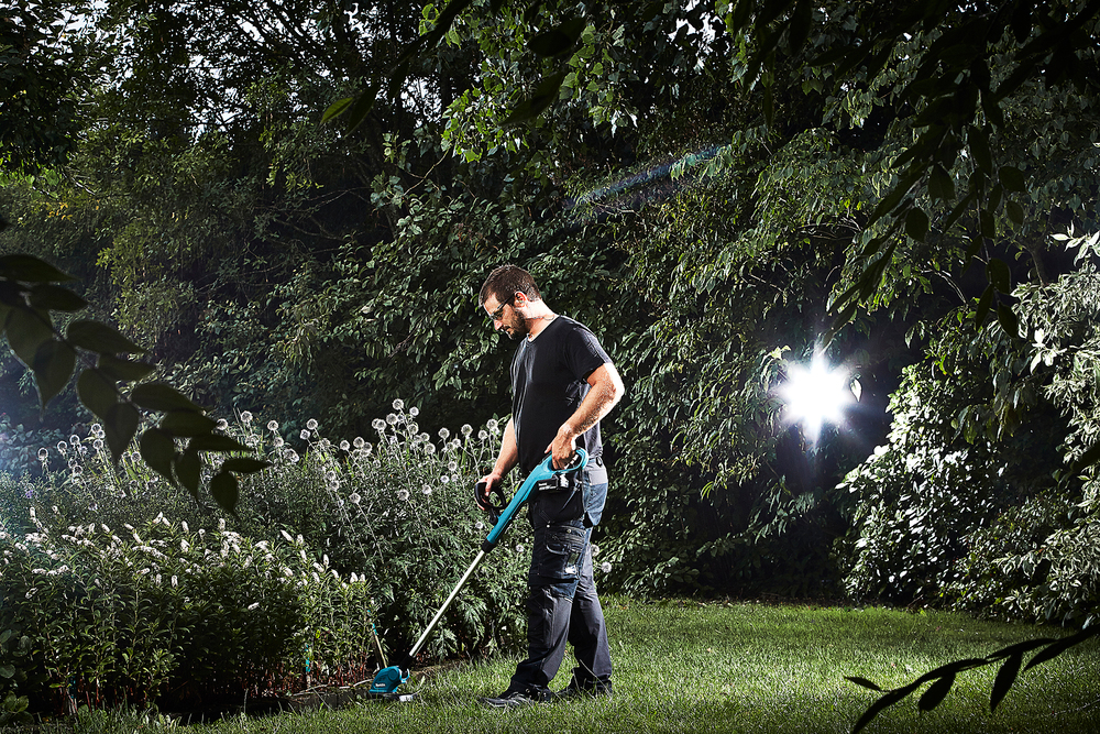 Ein Mann trimmt mit einem Makita Akku Rasentrimmer die Rasenkante um einer Hecke im Garten