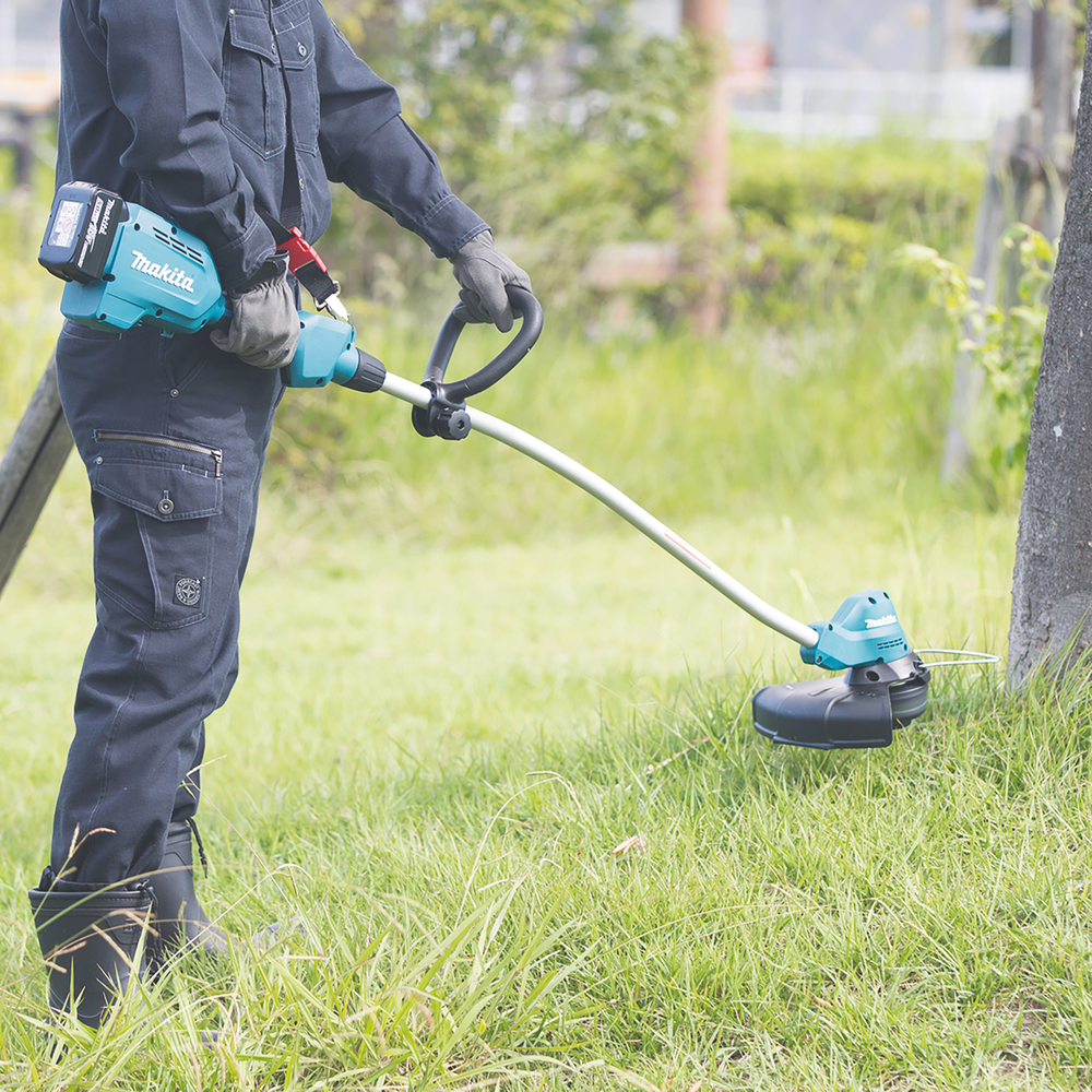ein Mann trimmt mit einem Makita Akku Rasentrimmer die Rasenkante um einen Baumstamm
