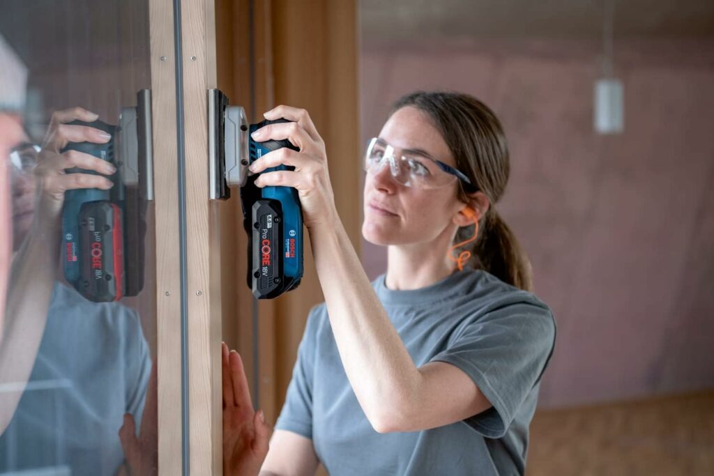Eine Frau schleift mit einem Bosch Professional Akku Schwingschleifer den Rahmen eines Fensters