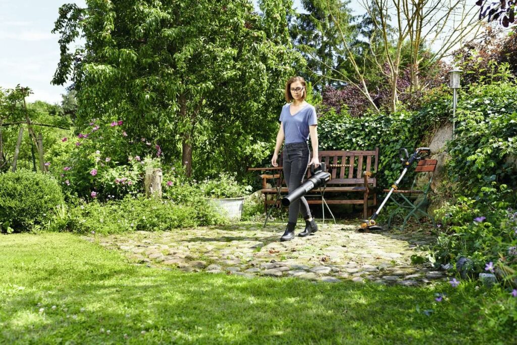 eine Frau nutzt einen Worx Akku Laubbläser um den Rasen ihres Gartens von Laub zu befreien